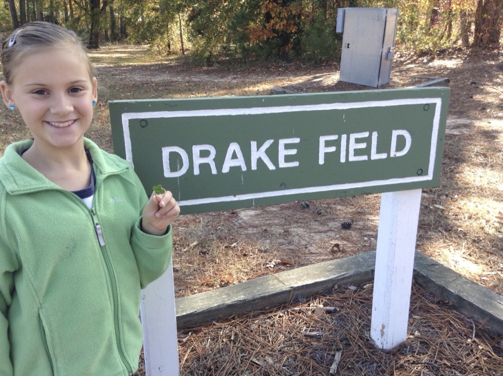 Addie with a clover by the Drake Field sign