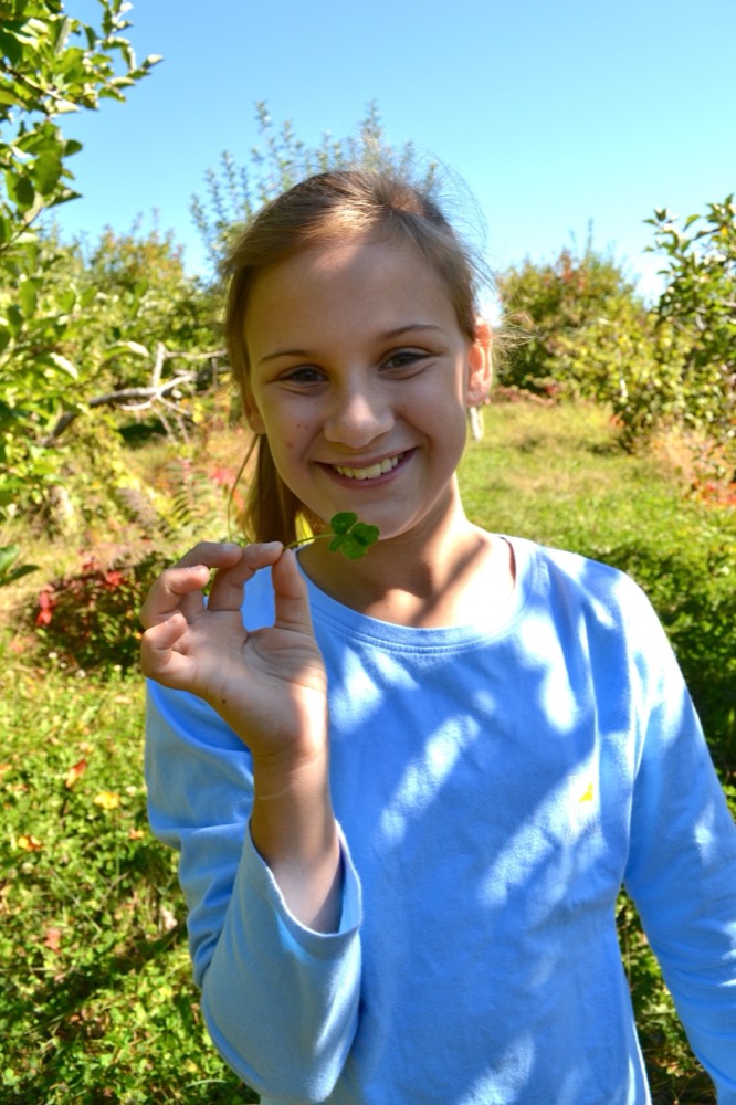 Young Addie holding a four-leaf clover in an orchard